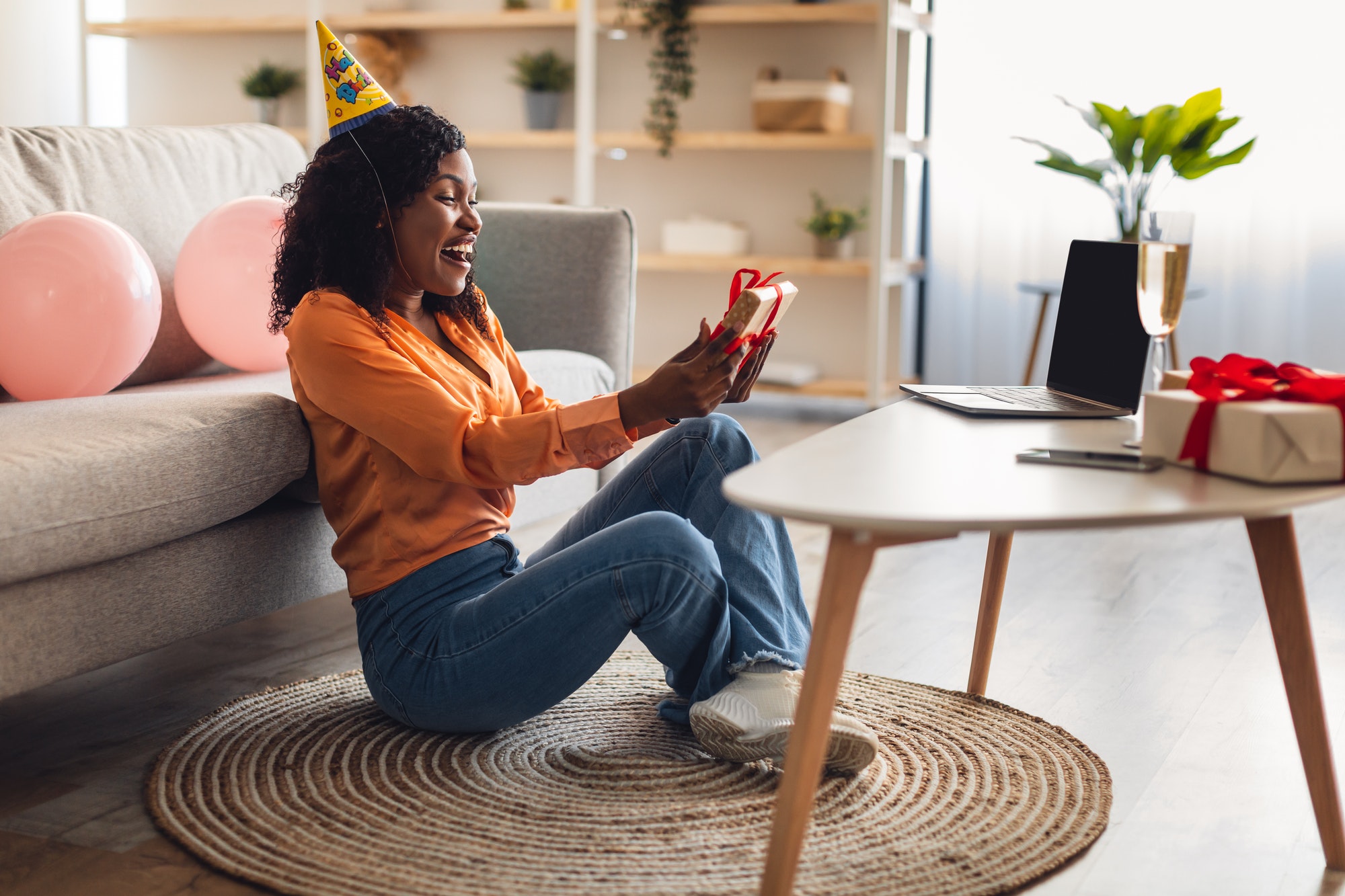 African Female Holding Gift Sitting At Laptop Video Calling Indoor