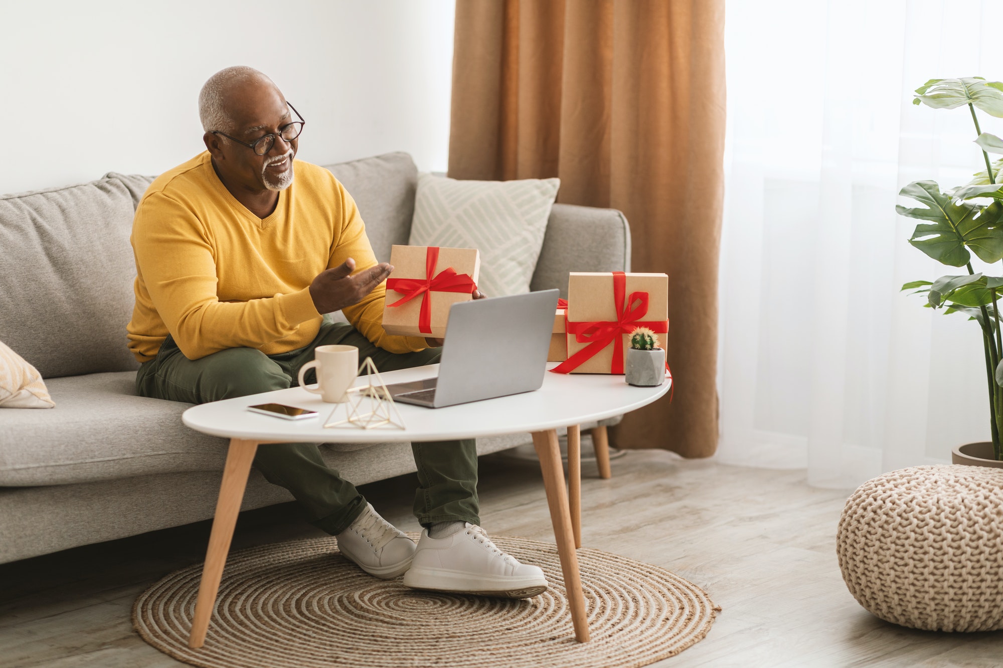 Senior Black Man Showing Gift To Laptop Video Calling Indoor