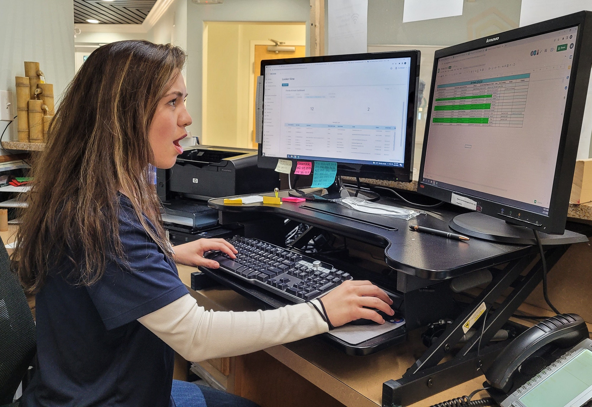 Young professional woman working in a condo real estate office at desk on computer.